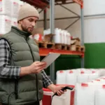 Petugas gudang memeriksa data persediaan menggunakan tablet di area penyimpanan